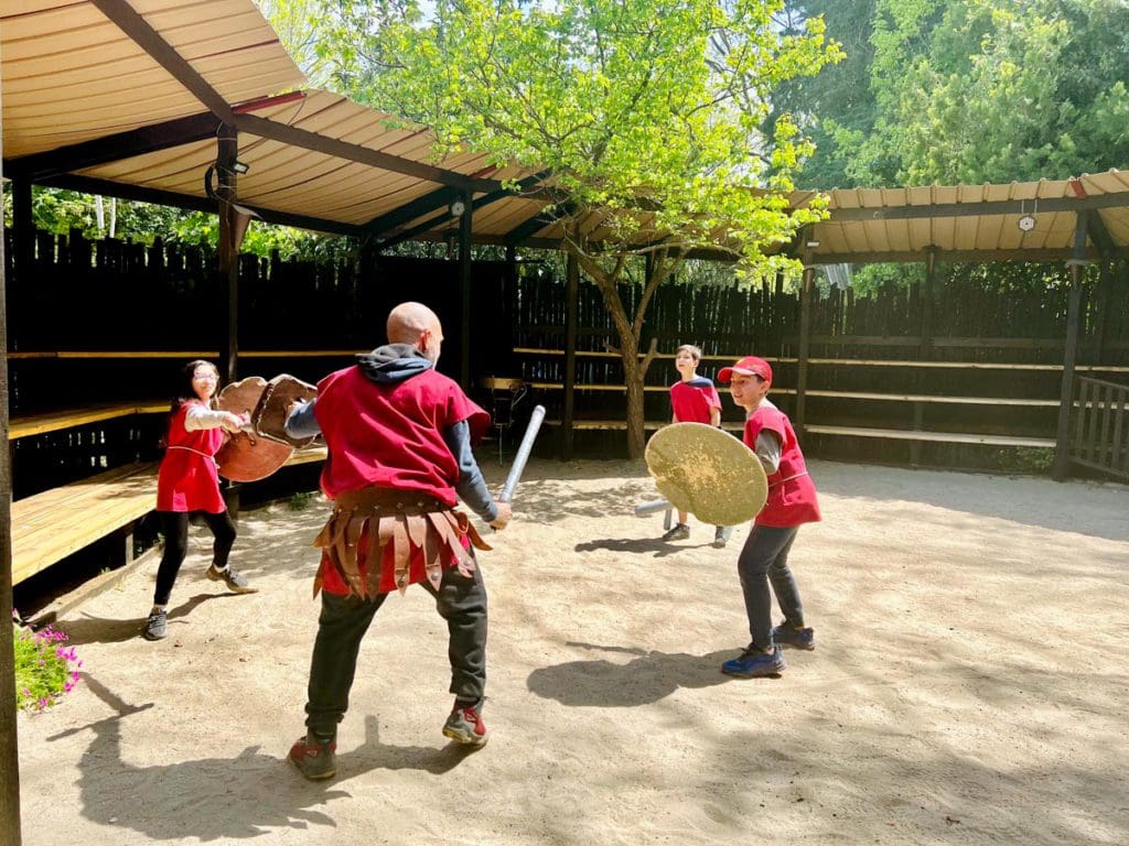 Two kids and two instructors practice gladiator fighting during a family-friendly class.
