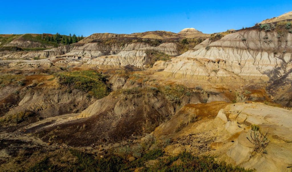 A landscape view of the Drumheller Badlands of Alberta, featuring multi-hued rock formations and blue skies.