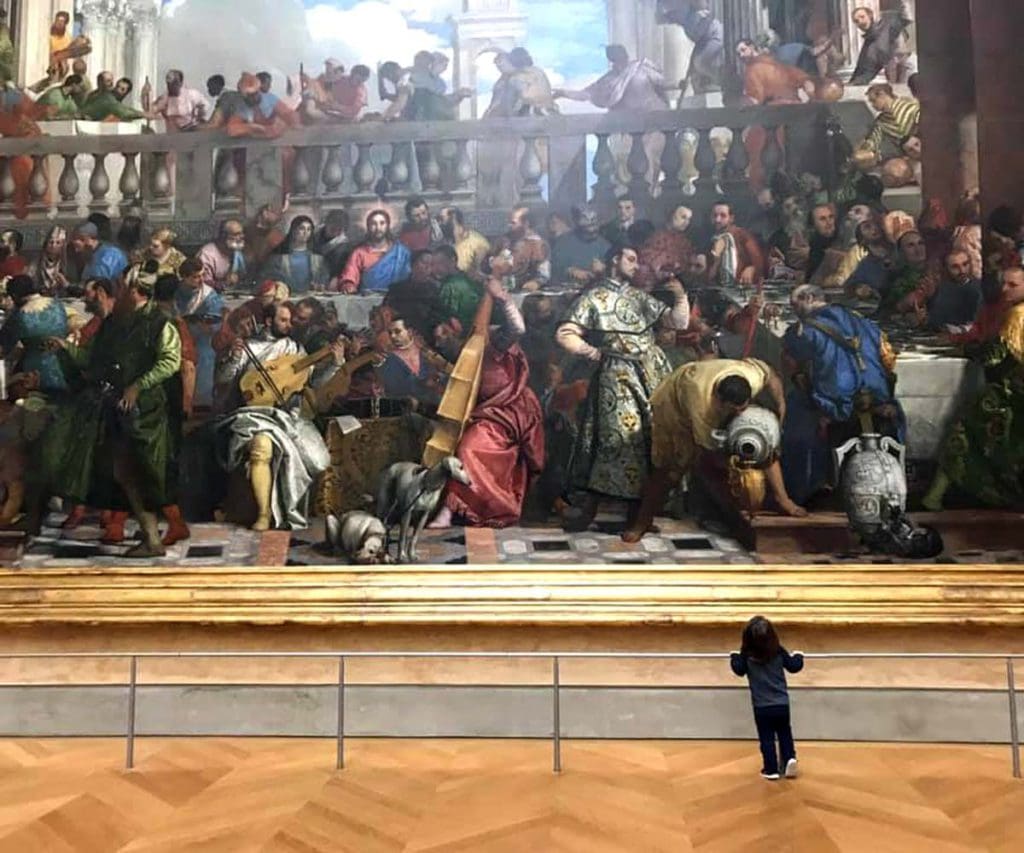 A young boy stands in front of a large painting at the Louvre Museum, one of the best museums in France with kids.