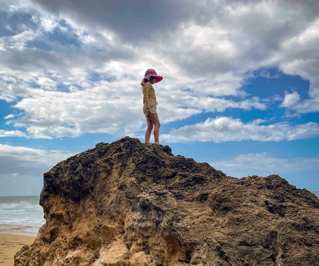A girl walks across the top of a huge boulder on the beach at Survival Beach.