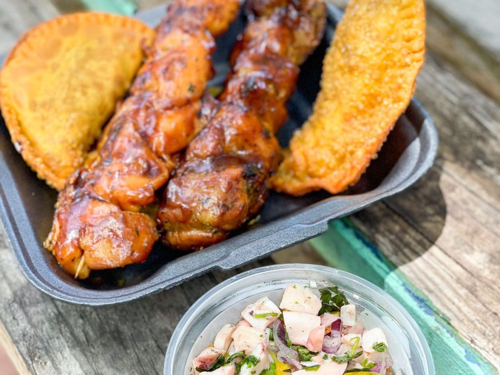 On a picnic table, a close up of Puerto Rican food, including pinchos, empanadas, and an octopus salad.