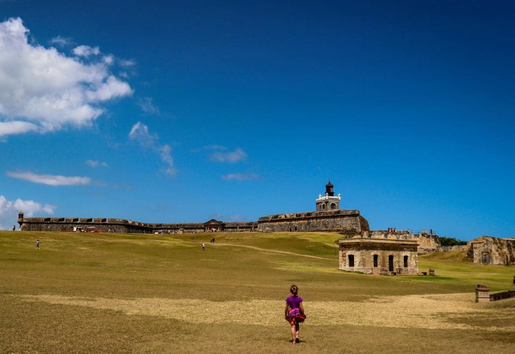 A young girl walks across the huge lawn toward San Felipe del Morro Castle in San Juan, a must stop on any Puerto Rico itinerary for families.
