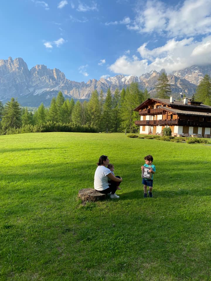 A mom and her young son play in a large green field with the Dolomite mountains in the distance.