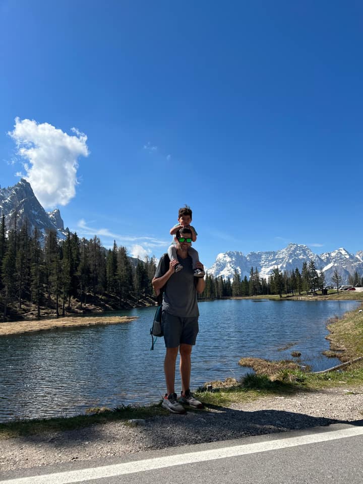 A dad holds his young son on his shoulders with Lake Garda behind them.