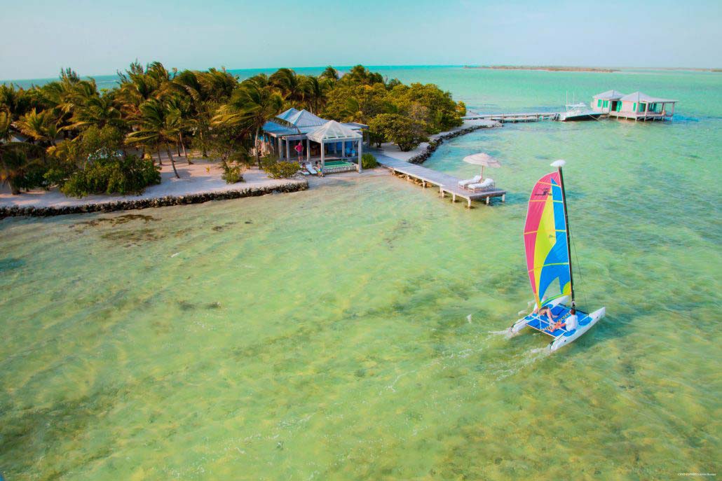 A sail boat passes by the boardwalk to Cayo Espanto Island Resort, one of the best Belize resorts for a family vacation! 
