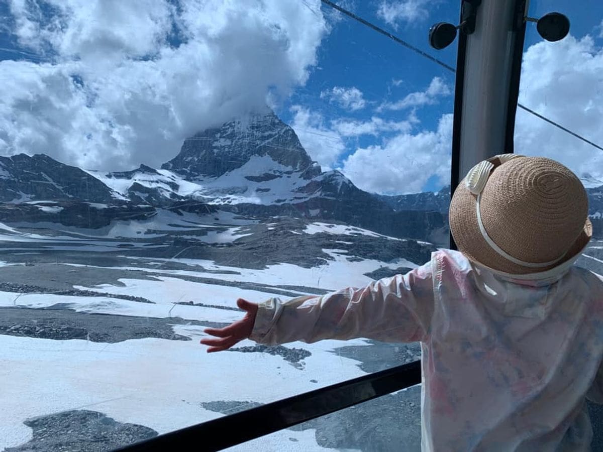 A young girl stretch out her arms as she looks at the Matterhorn from a gondola window near Zermatt, one of the best mild weather European destinations for a family summer vacation.