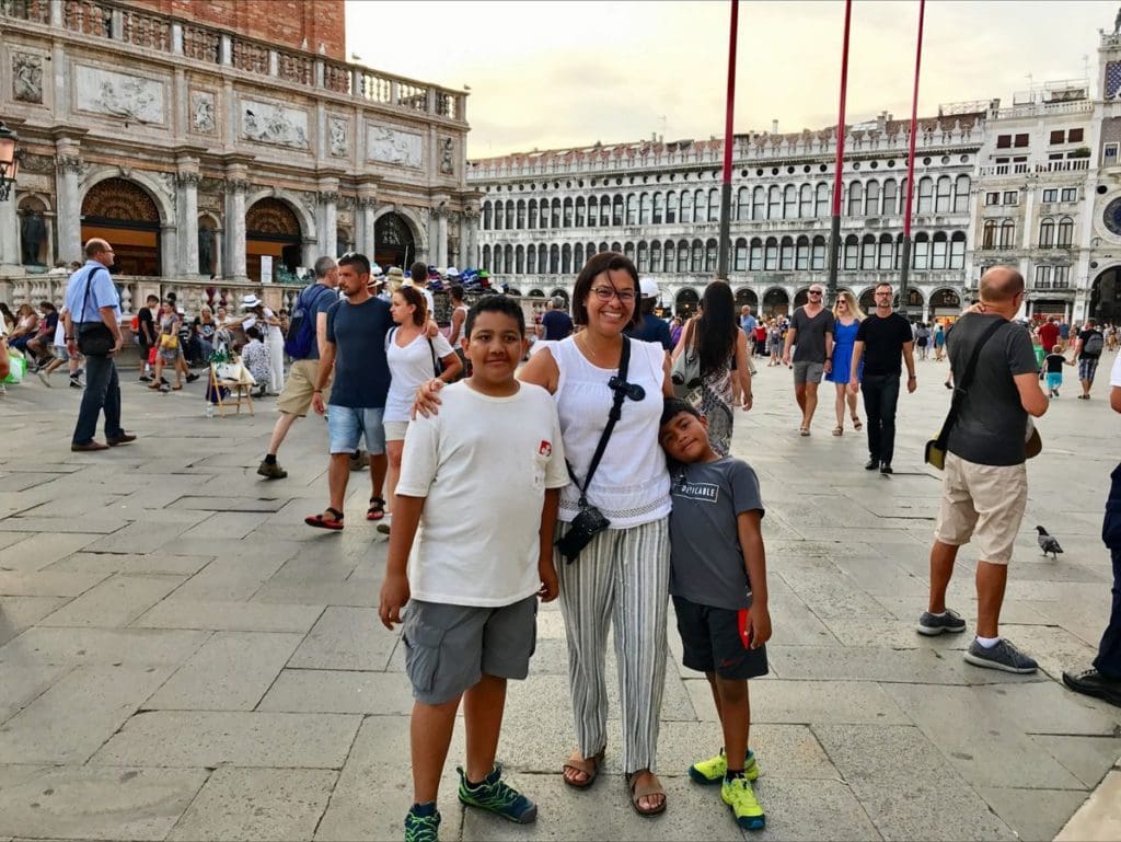 A mom and her two sons stand together with Piazza San Marco behind them.