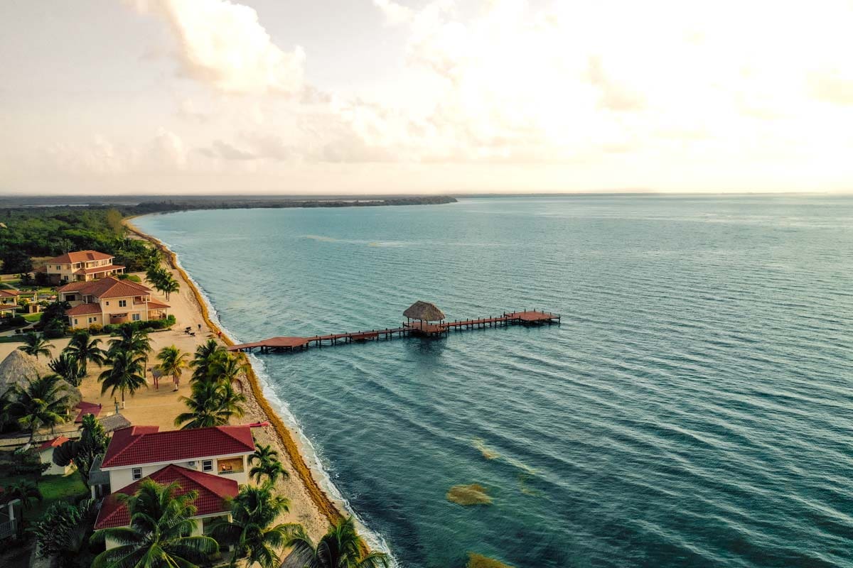 An aerial view of Hopkins Bay Belize, a Muy’Ono Resort, featuring its long pier and stretch of beach.