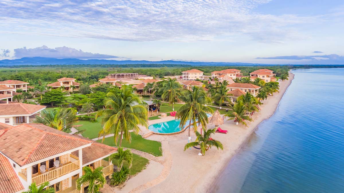 An aerial view of Hopkins Bay Belize, a Muy’Ono Resort, featuring a long stretch of beach, swaying palms, and stunning resort buildings at one of the best Belize resorts for a family vacation.