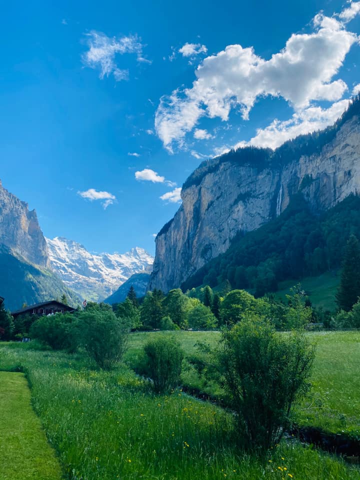 A large green field with mountain views near Lauterbrunnen, one of the best mild weather European destinations for a family summer vacation.