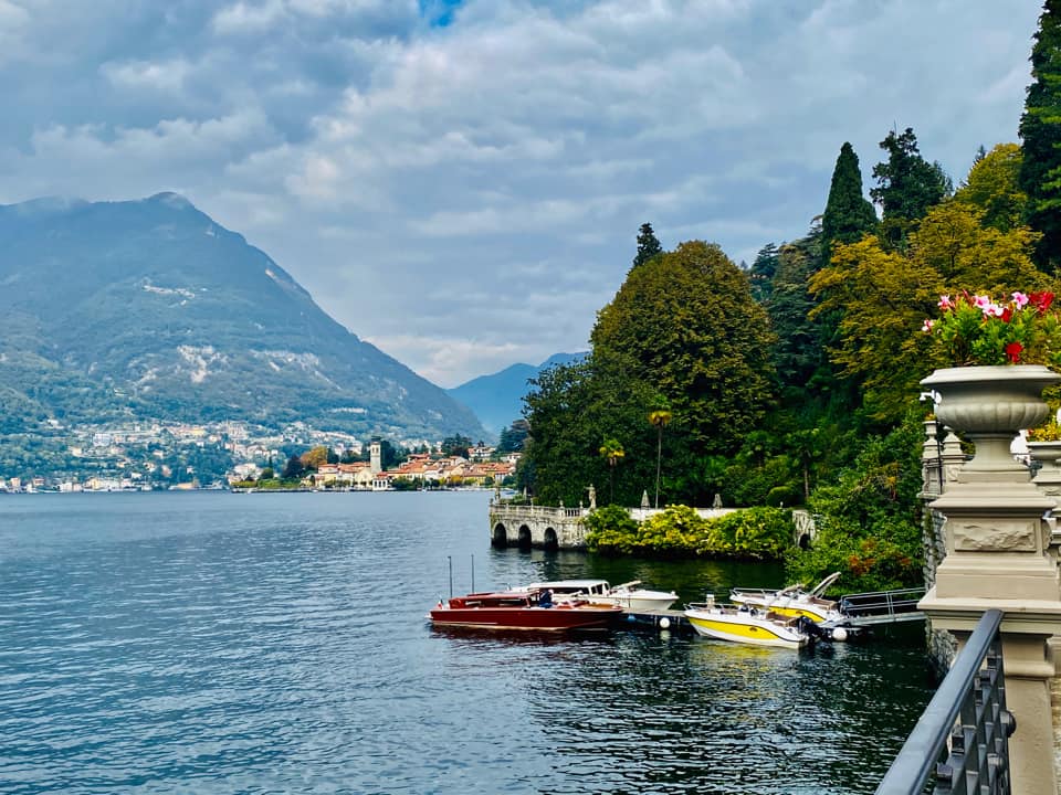 Lake Como, with mountains in the distance, and a dock with boats on the side.