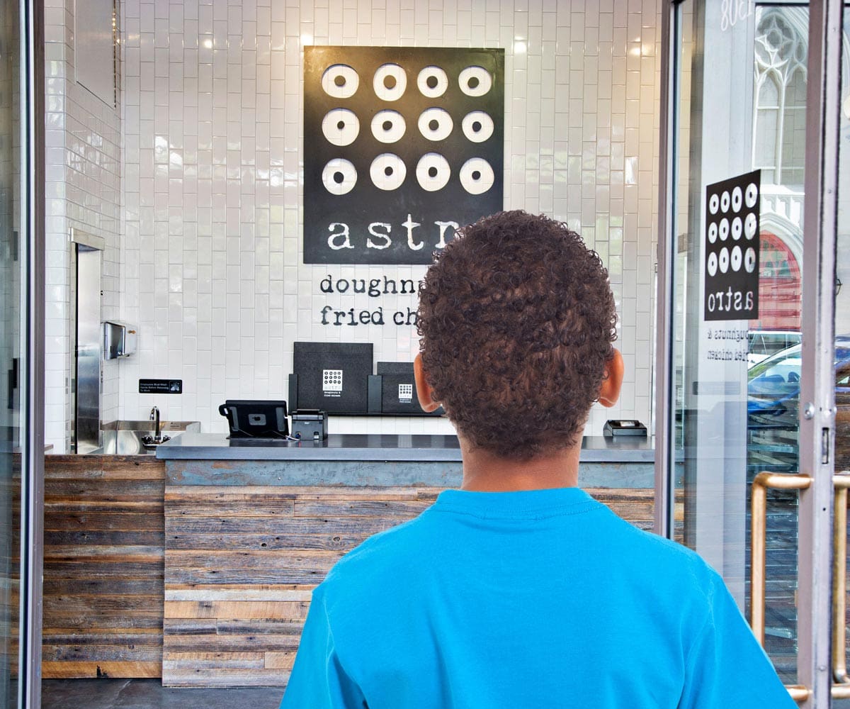 A young boy of color, wearing a blue shirt, looks into Astro Doughnuts & Fried Chicken, one of the best DC dessert places for families.