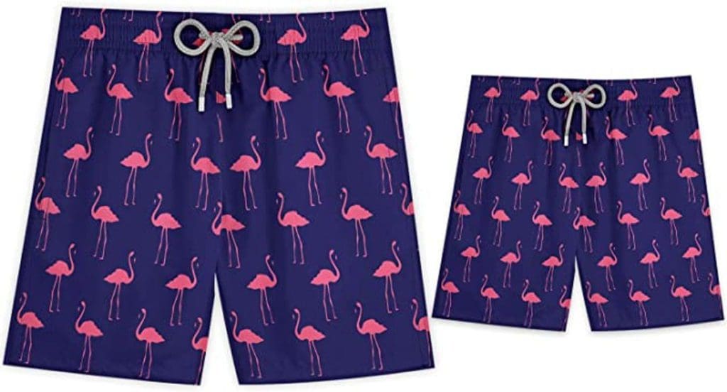 Product shot for a matching set of Stivali swim trunks for an adult in child, in navy with pink flamingos.
