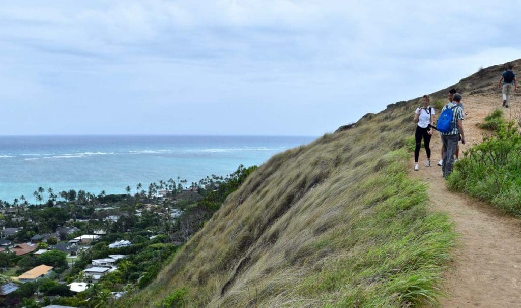 Several people hike along the the Lanikai Pillbox Hike, hiking along a ridge over looking the water.