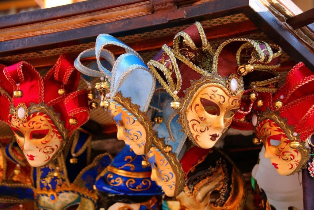 Several vibrant Venetian masks hang from a shop.