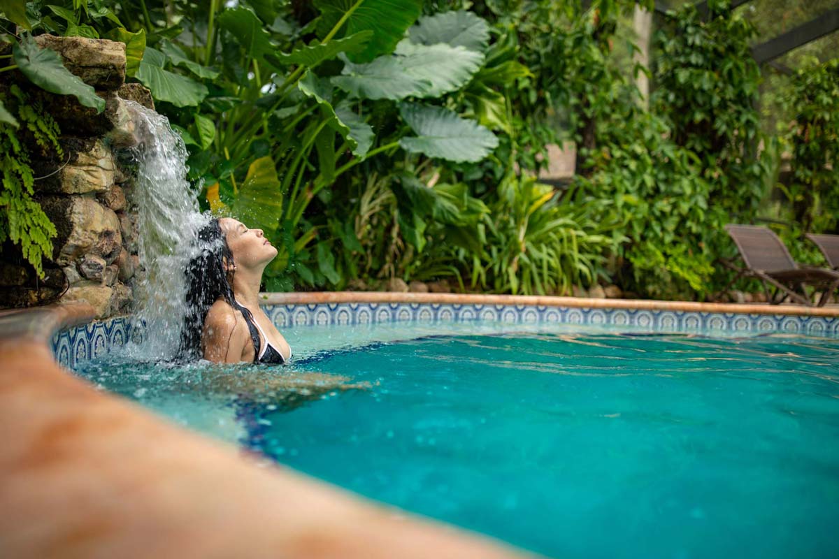 A woman leans her head back into a small waterfall feature at the pool at Chan Chich Lodge.