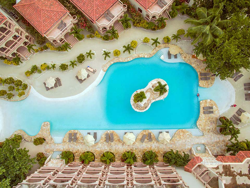 An aerial view of the large pool at Coco Beach Resort, with the surrounding pool deck awaiting guests.