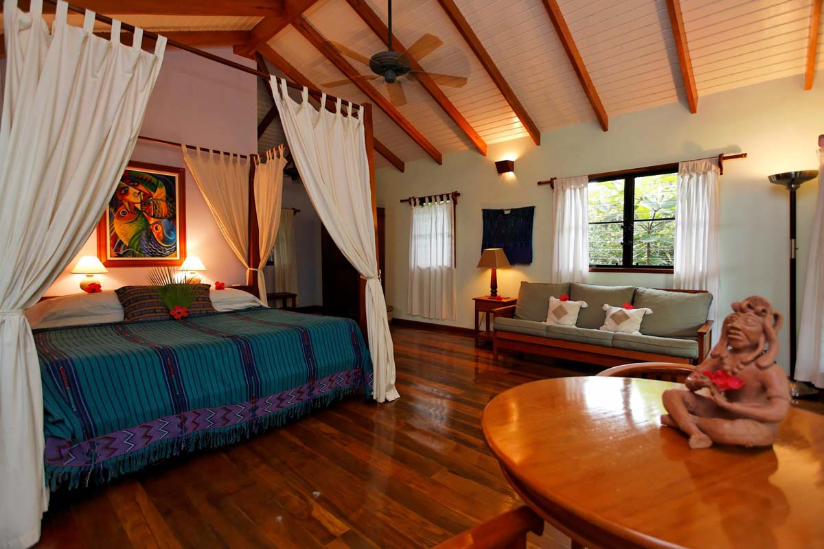 Inside a tropical room at Hamanasi Adventure & Dive Resort, featuring a large bed, table, and couch.