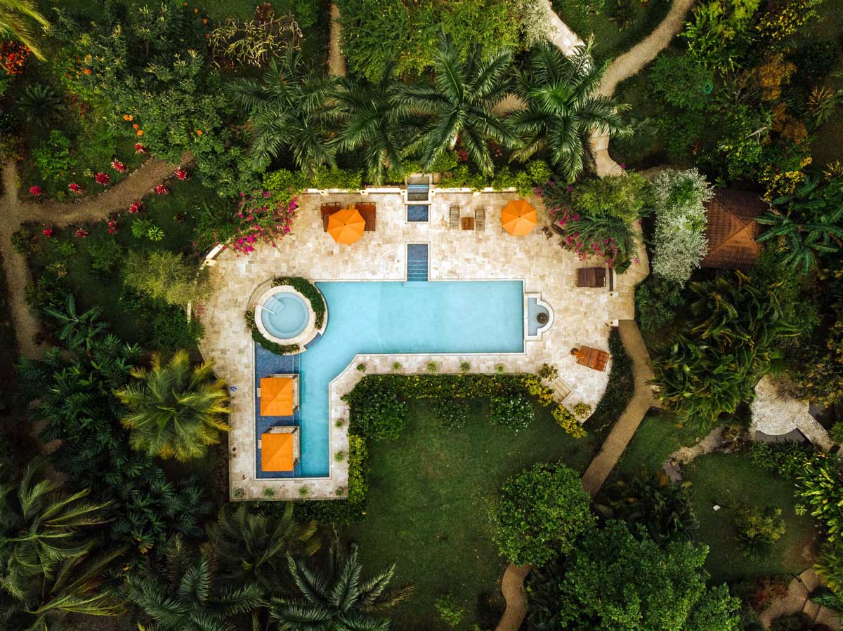 An aerial view of the pool an surrounding pool deck, flanked by rainforest, at Sleeping Giant Rainforest Lodge.