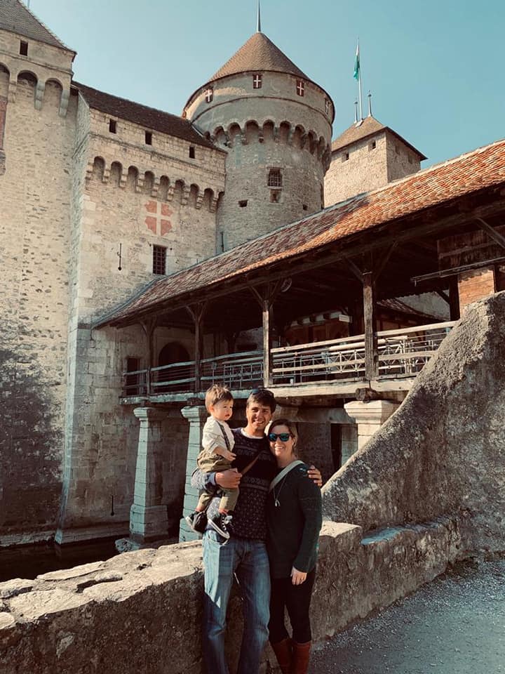A family of three stands together in front of the castle in Montreux, one of the best towns and villages to visit with your family in Switzerland.