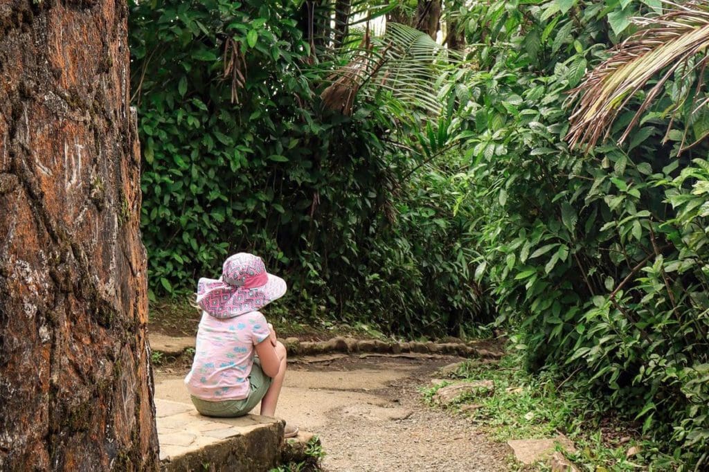 A young girl sits near the base of a tower, while taking a rest from hiking in El Yunque National Forest, a must stop on any Puerto Rico itinerary for families.