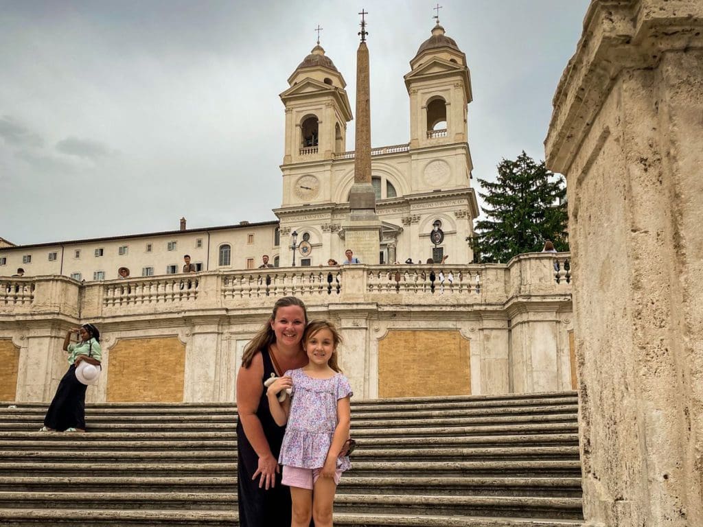 A mom and her daughter stand together on the Spanish Steps, with the Spanish embassy in the distance, this is one of the best neighborhoods to stay in Rome with kids.