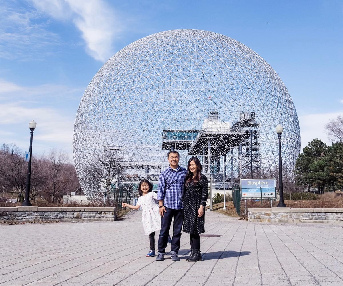 Two parents and their young daughter stand in front of Montreal's Biosphere.