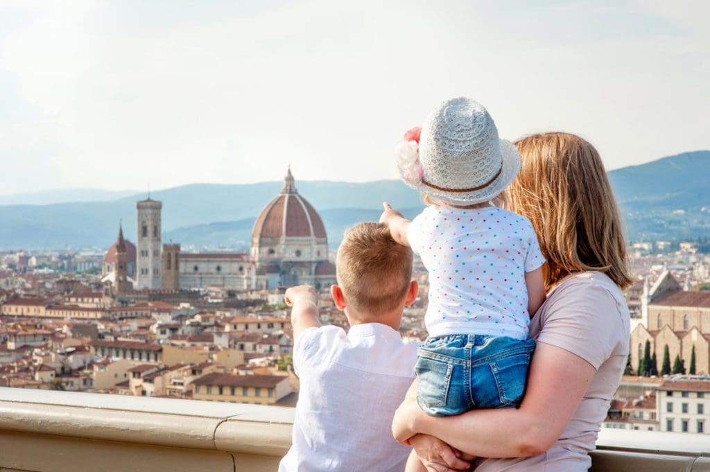 A mom and her two kids look out onto a Florence skyline, while one young one boy points at the Duomo