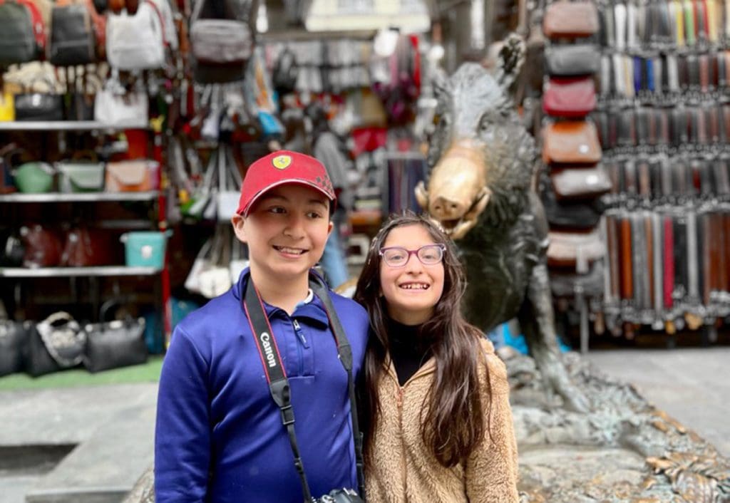 Two kids smile in front of the infamous Fontana Del Porcellino, learning about things to do in Florence is an important part of knowing all about Italy with kids.