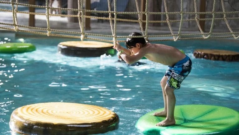 A young boy crosses the lily pad bridge in the indoor waterpark at Great Wolf Lodge in Ontario.