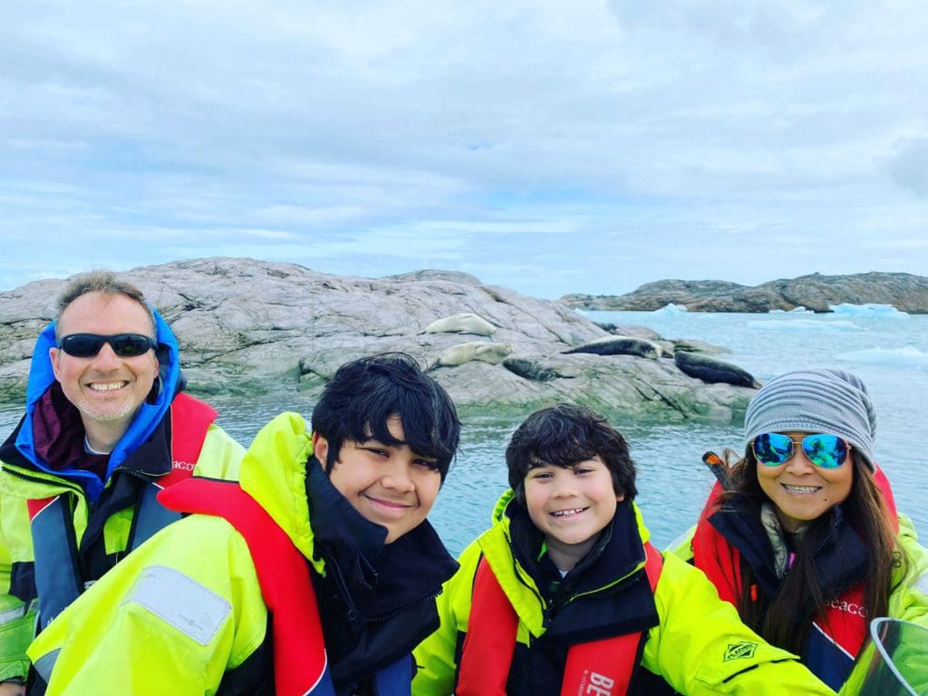 A family of four smiles together, all wearing bright green jackets while on a outdoor tour in Iceland.
