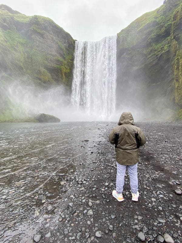A man with his back turned stands in front of an Icelandic waterfall.
