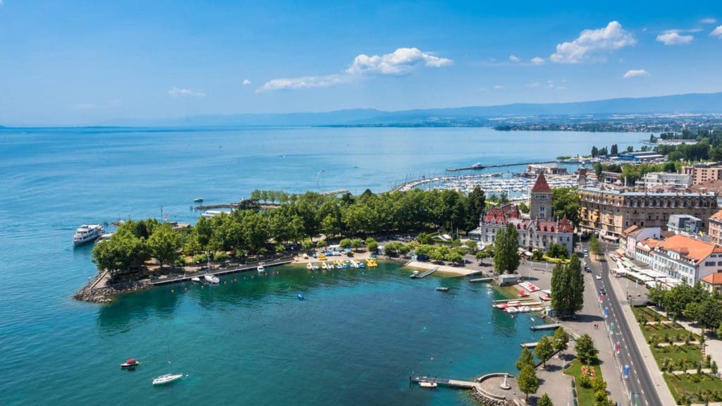 An aerial view of Lausanne, one of the best towns and villages to visit with your family in Switzerland, featuring a large lake and cozy town nestled along the lake.