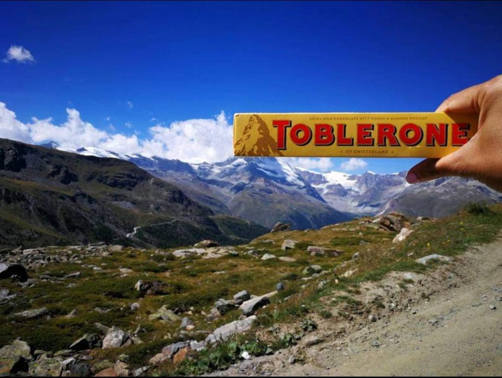 A woman's hand holds a Toblerone over the Matterhorn to complete the image of the mountain near Zermatt, one of the best towns and villages to visit with your family in Switzerland.