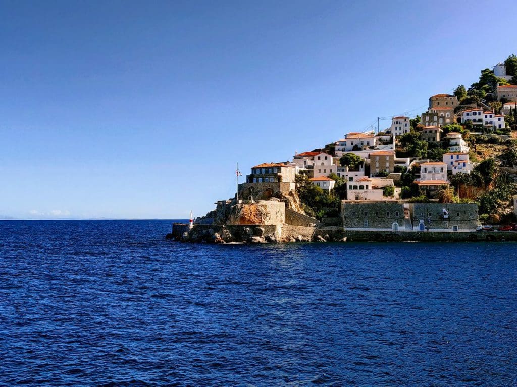Houses set upon an upward slope of the island of Hydra, surrounded by sea and sky.