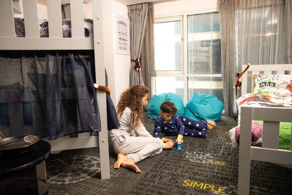 Two kids play with toys between their beds in the kid's room at Park Plaza London Riverbank, one of the best London Hotels for Families.