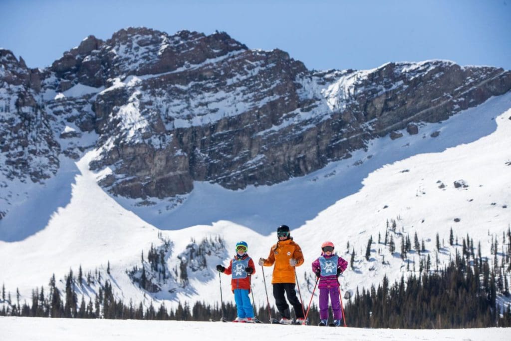 Two kids stand near a ski school instructor at Ski Alta atop the mountain with a snow all around them at one of the best Thanksgiving destinations in the United States for families.