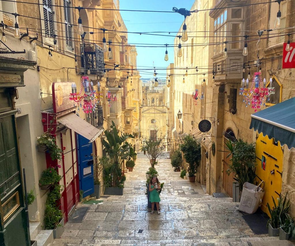 A young girl stands in the center of a charming street, with stairs leading down in Malta, knowing the streets aren't always stroller-friendly is this is one of our best tips for visiting Malta with kids.