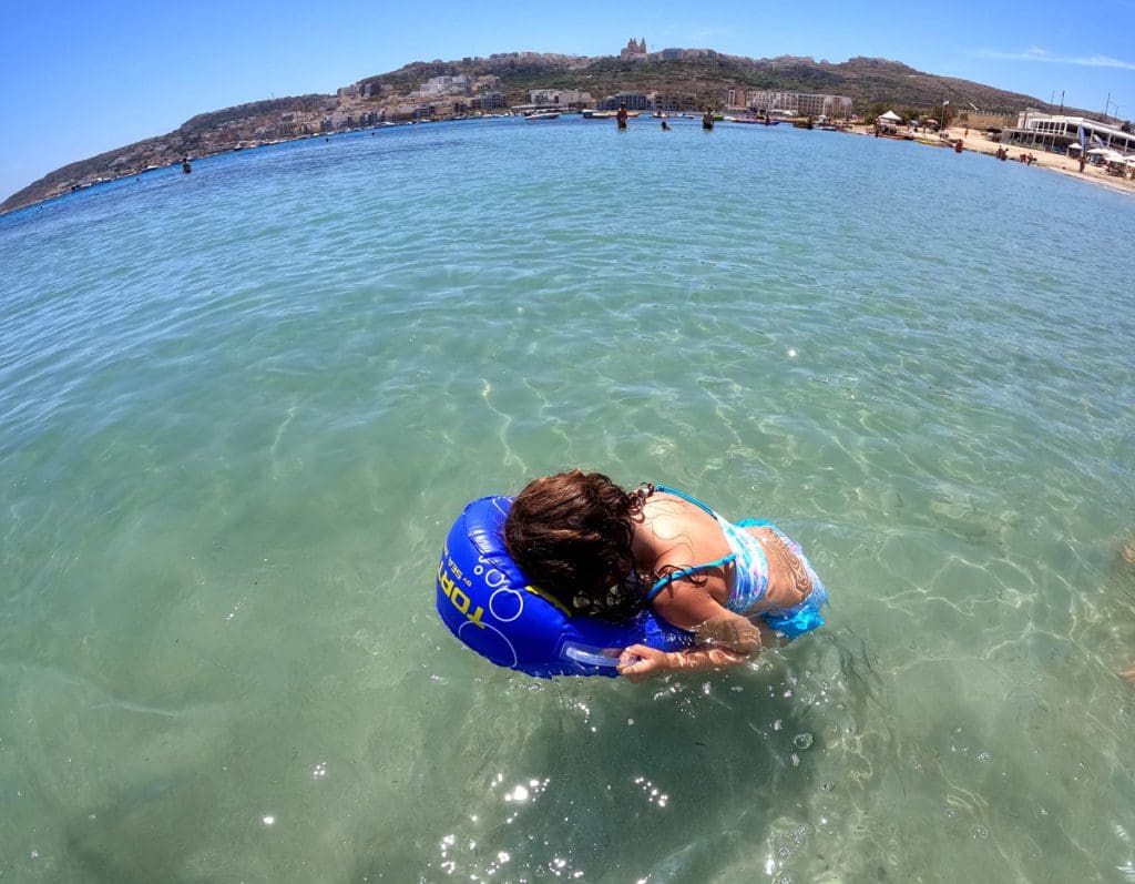 A young girl looks through a toy into the water off-shore from the island of Malta, packing the right beach gear is this is one of our best tips for visiting Malta with kids.