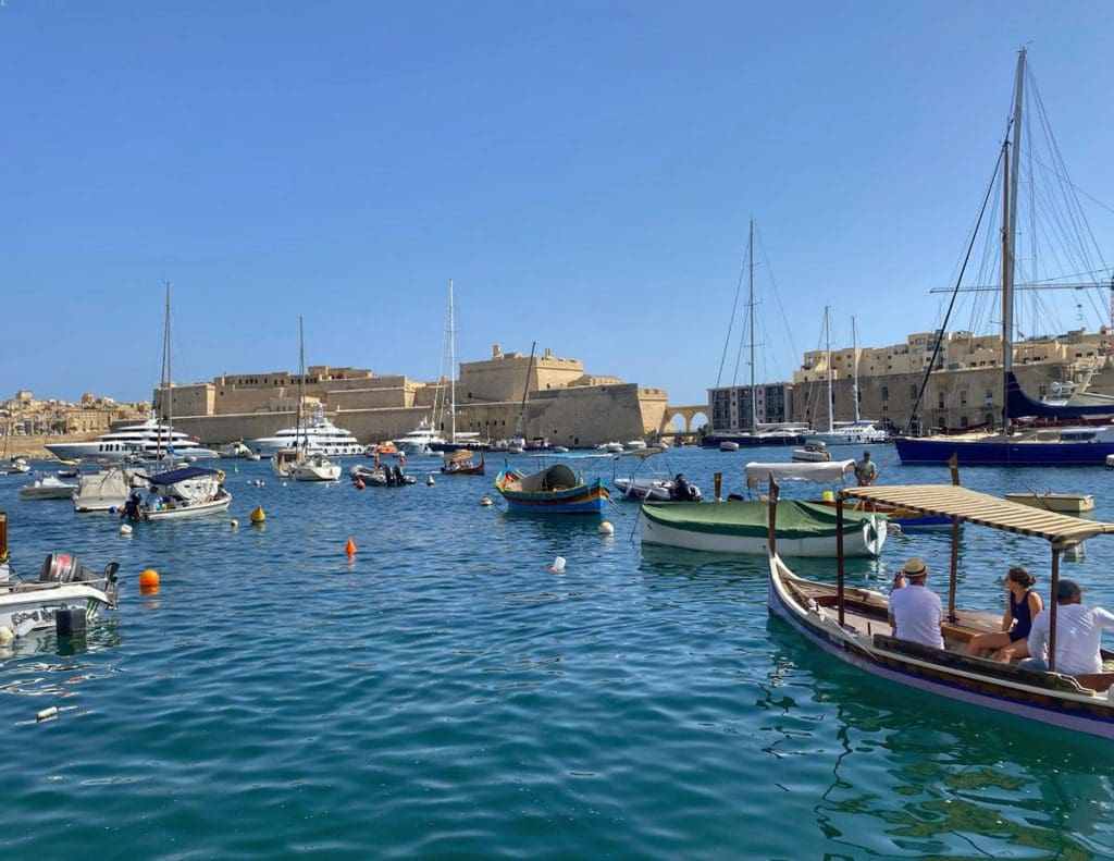 A bay of anchored boats off-shore from a historic port in Malta.