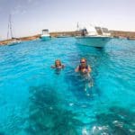 A mom and her young daughter swim in crystal blue waters near a boat off-shore in Malta.