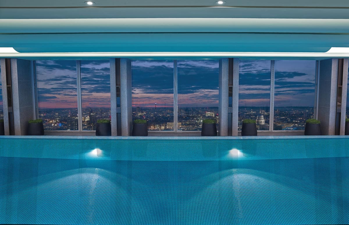 The indoor pool at Shangri La at the Shard, with floor to ceiling windows opposite the pool featuring a night skyline of London.