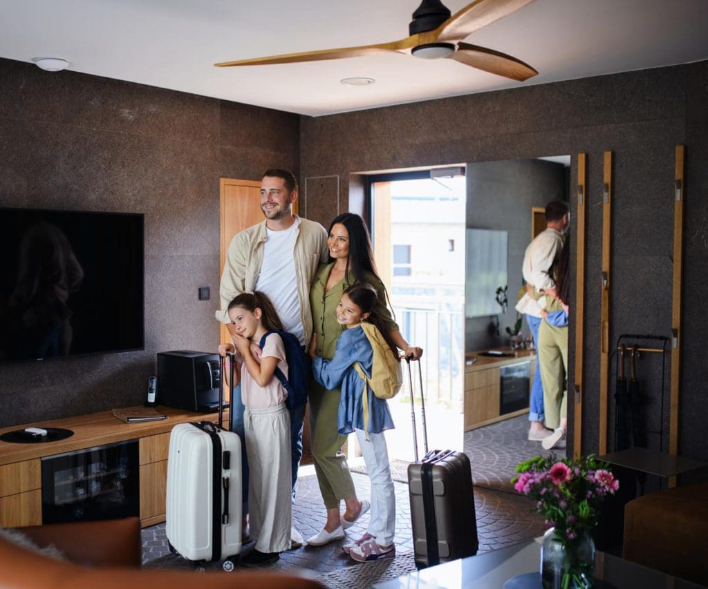 A family of four stands together in the entrance of a home rental with their luggage, knowing where to stay can help plan a family ski trip on a budget.