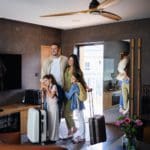 A family of four stands together in the entrance of a home rental with their luggage.