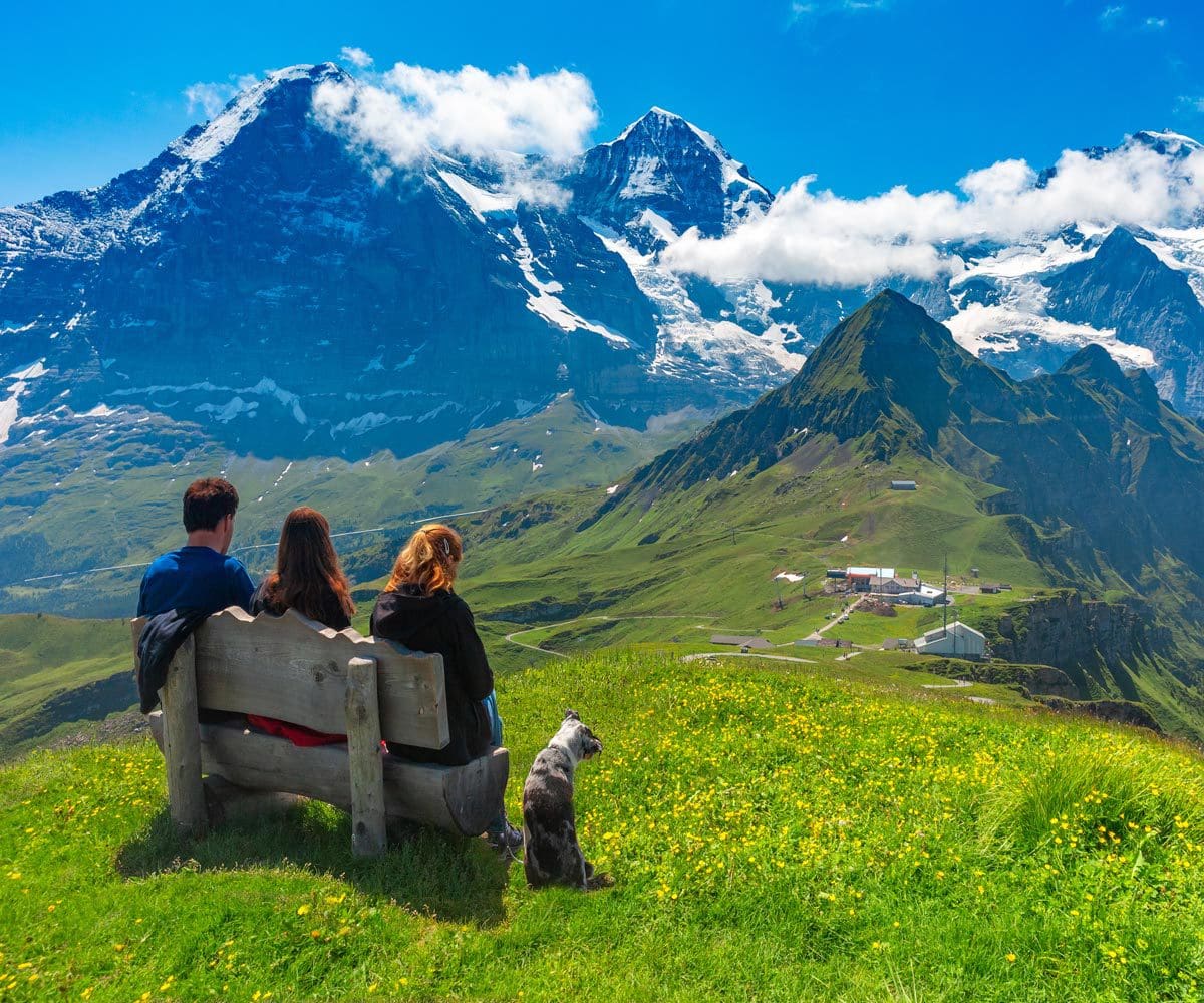 A family of three sits together on a bench, while taking in a mountain view near Wengen.