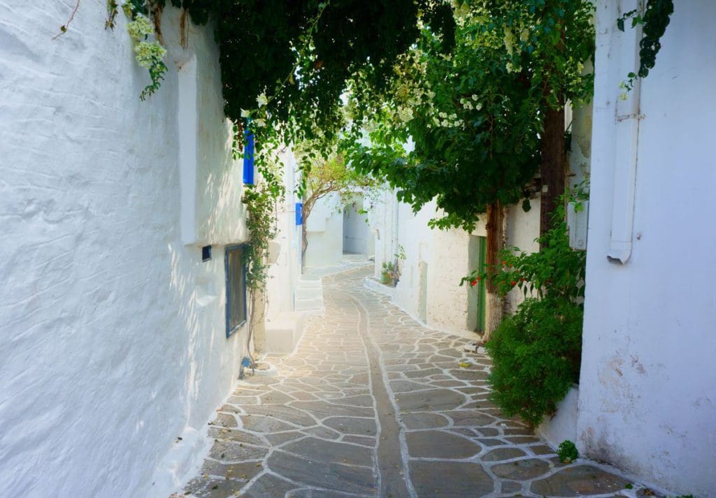 A narrow road leads through whitewashed buildings, with lush greenery overhead, on the island of Paros, one of the best Greek islands for families.