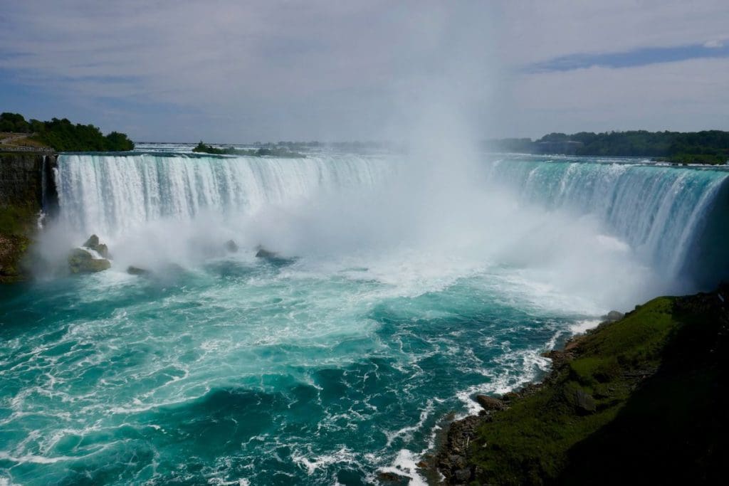 A view of Niagara Falls from the Canadian side, with water rushing over the falls and a large spray.