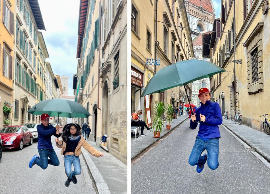Left Image: Two kids jump together with an umbrella on a Florentine street. Right Image: A young boy jumps while holding a green umbrella on a street in Florence.