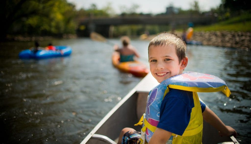 A little boy turns to look at the camera, while canoeing down the Huron River with his family near Ann Arbor, one of the best places to visit in Michigan with kids.