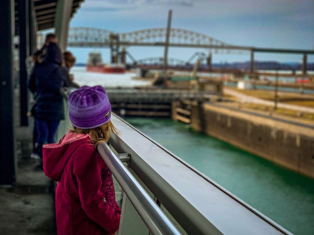 A young girl looks down the Soo Locks toward and oncoming ship moving through the locks.